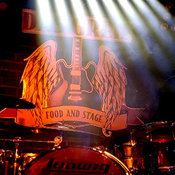 Greif-Logo einer E-Gitarre mit Flügeln an der Wand hinter einem Schlagzeug