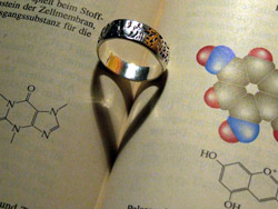 Der Schatten eines Ringes in der Falz eines aufgeschlagenen Physikbuches formt ein Herz